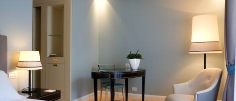A hotel room with a bed, a desk, a chair, a lamp, and a potted plant.