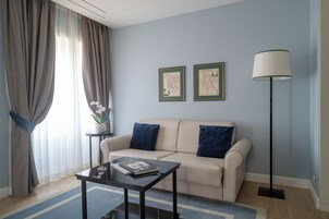 En stue med sofa, sofabord, lampe og to indrammede kort på væggen.