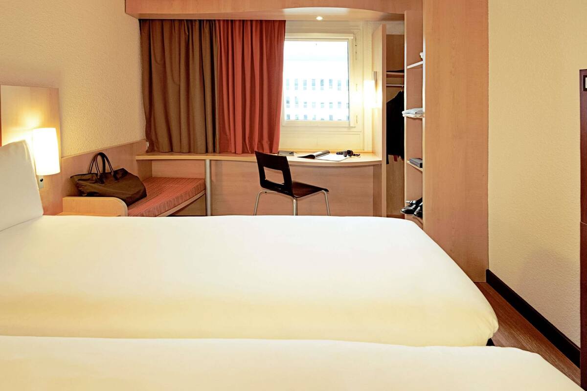 Une chambre d’hôtel avec un grand lit, un bureau avec une chaise, une fenêtre avec des rideaux et une armoire.