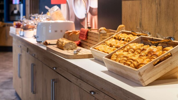 Un comptoir de buffet proposant une variété de produits de boulangerie, notamment du pain et des viennoiseries, ainsi qu’une machine à café.