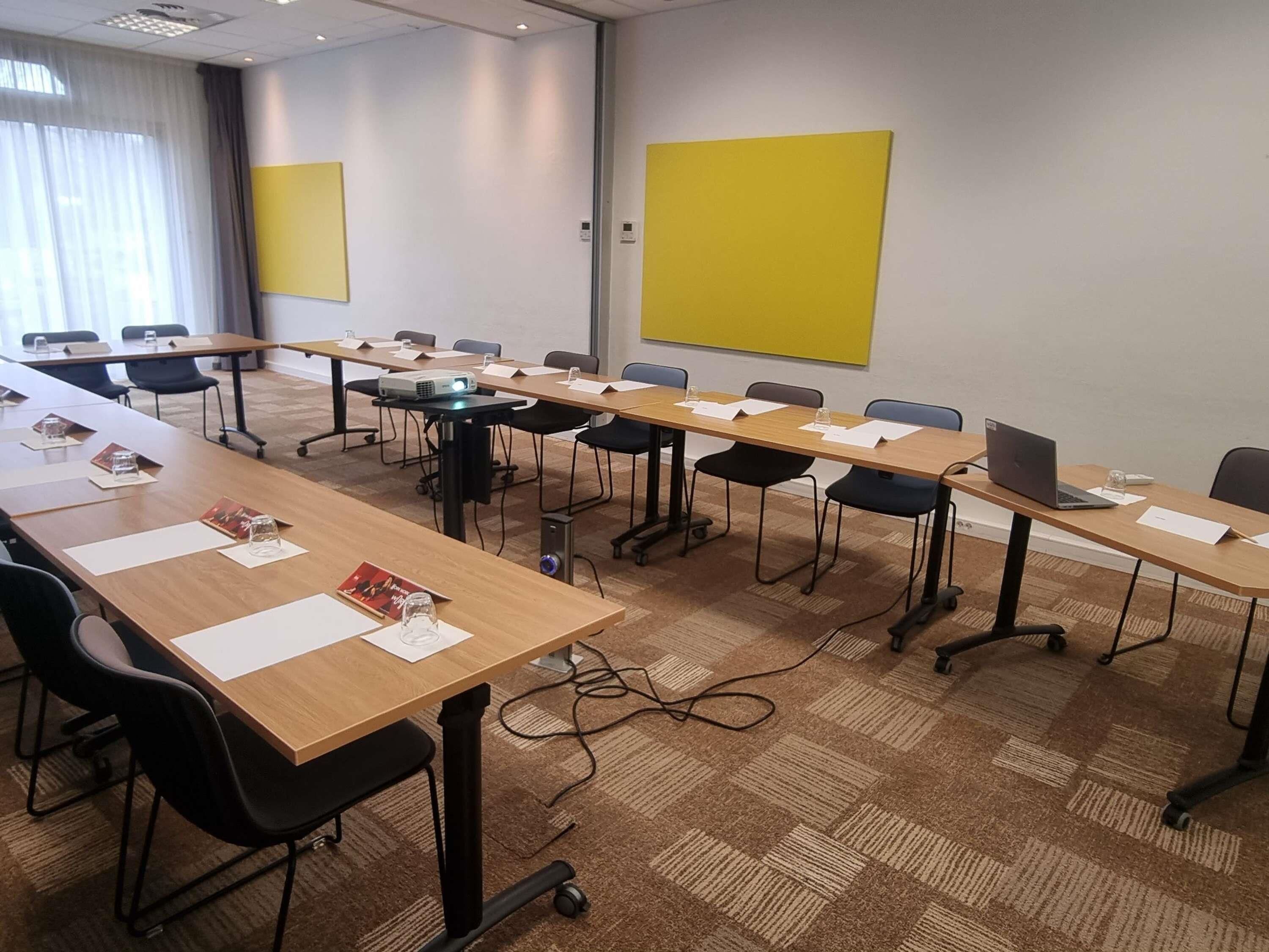 A conference room with long tables, chairs, a projector, and a yellow accent wall.