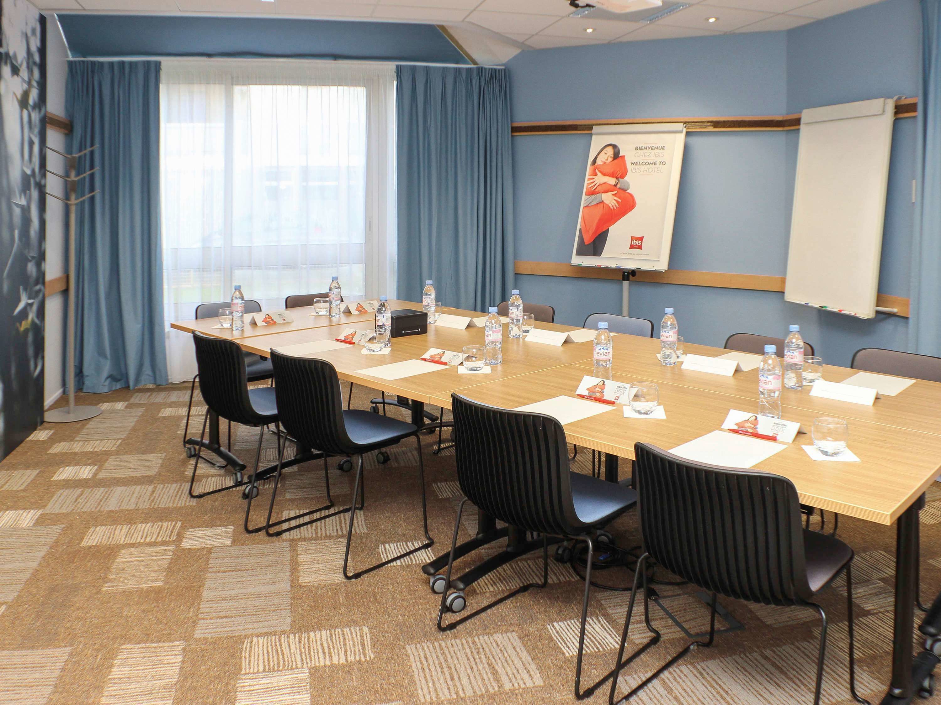 Une salle de conférence équipée d’une longue table, de chaises, de bouteilles d’eau, de porte-noms et d’un écran de projection.