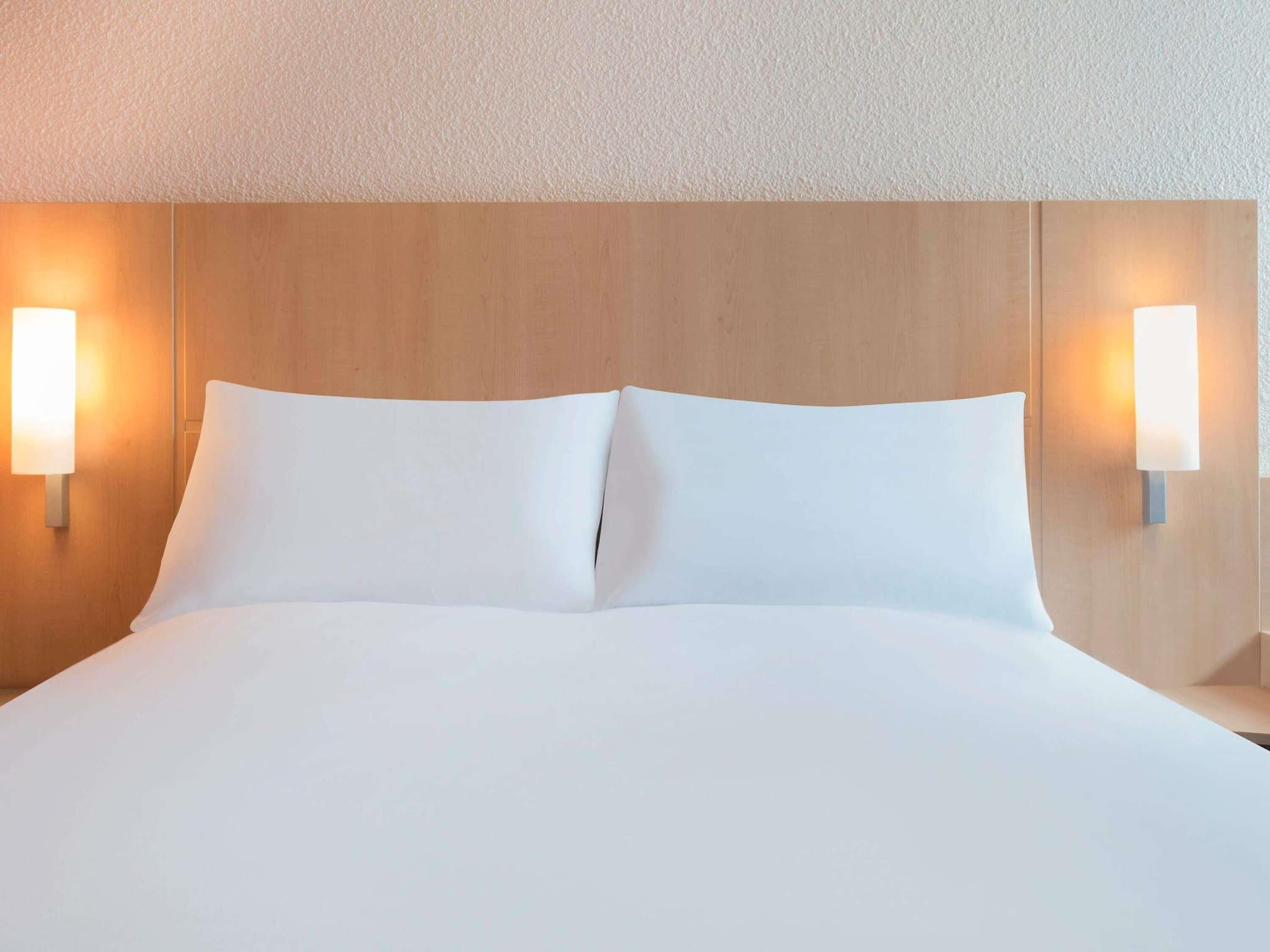 Una habitación de hotel con una cama grande, dos lámparas de noche y un cabecero de madera.