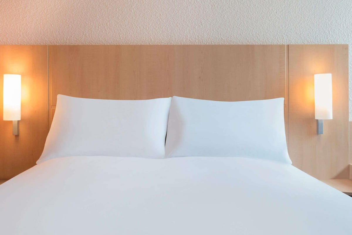 A hotel room with a large bed, two bedside lamps, and a wooden headboard.