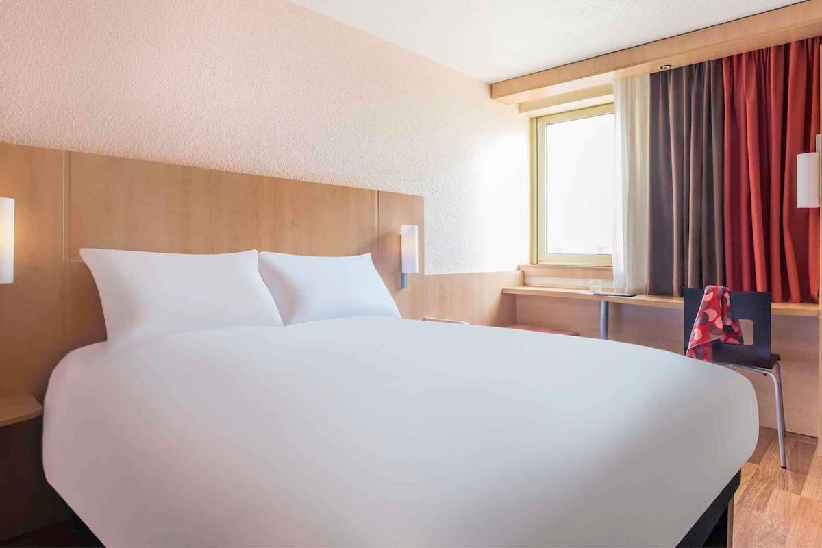 Une chambre d’hôtel avec un grand lit, un bureau, une chaise et une fenêtre avec des rideaux.