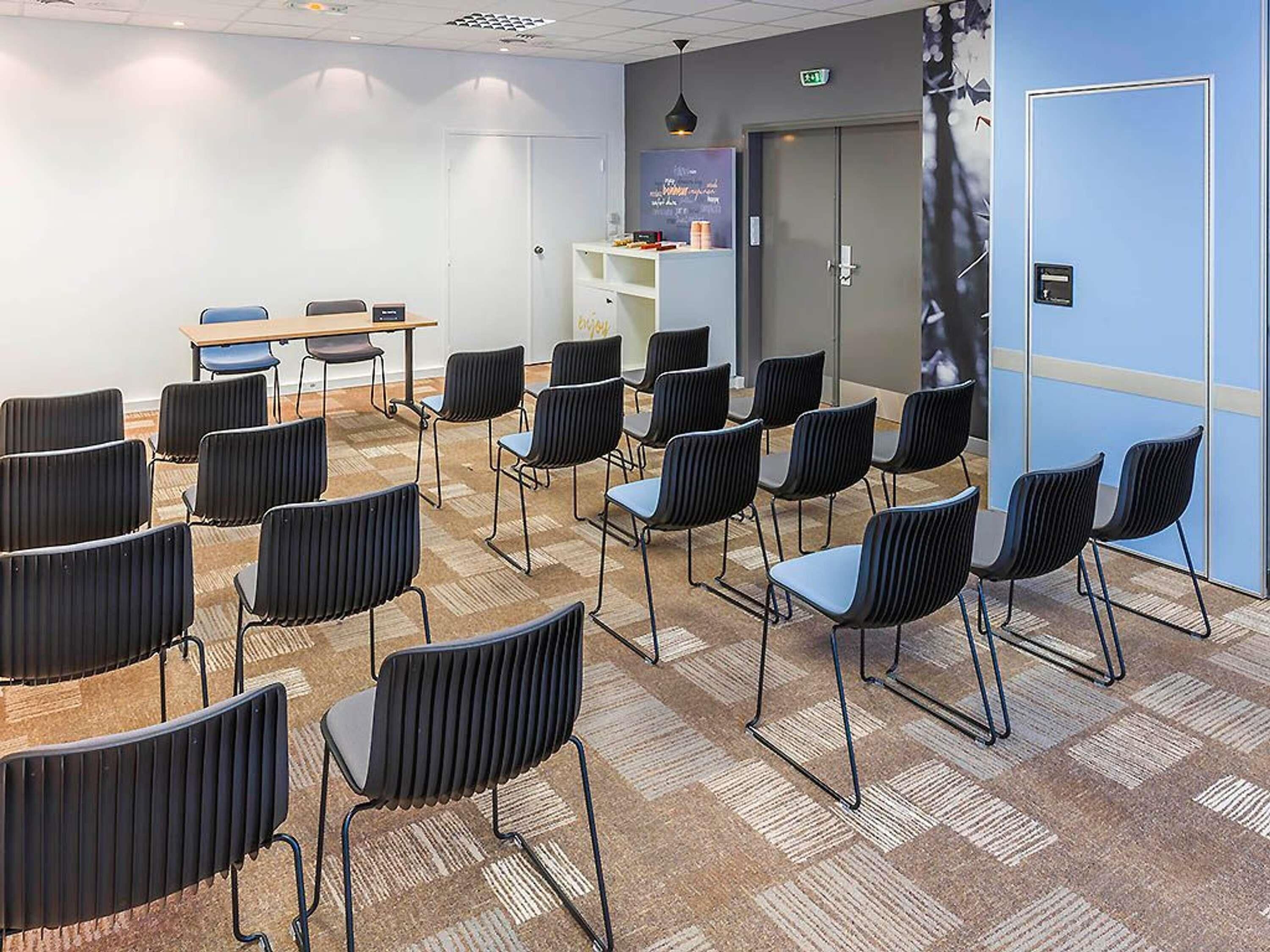 A conference room with rows of chairs, a whiteboard, and a door with a blue frame.