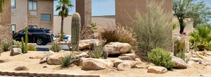 A desert garden with cacti and rocks, a parking lot with cars, and a building in the background. - Travelodge by Wyndham Lake Havasu (Lake Havasu City)