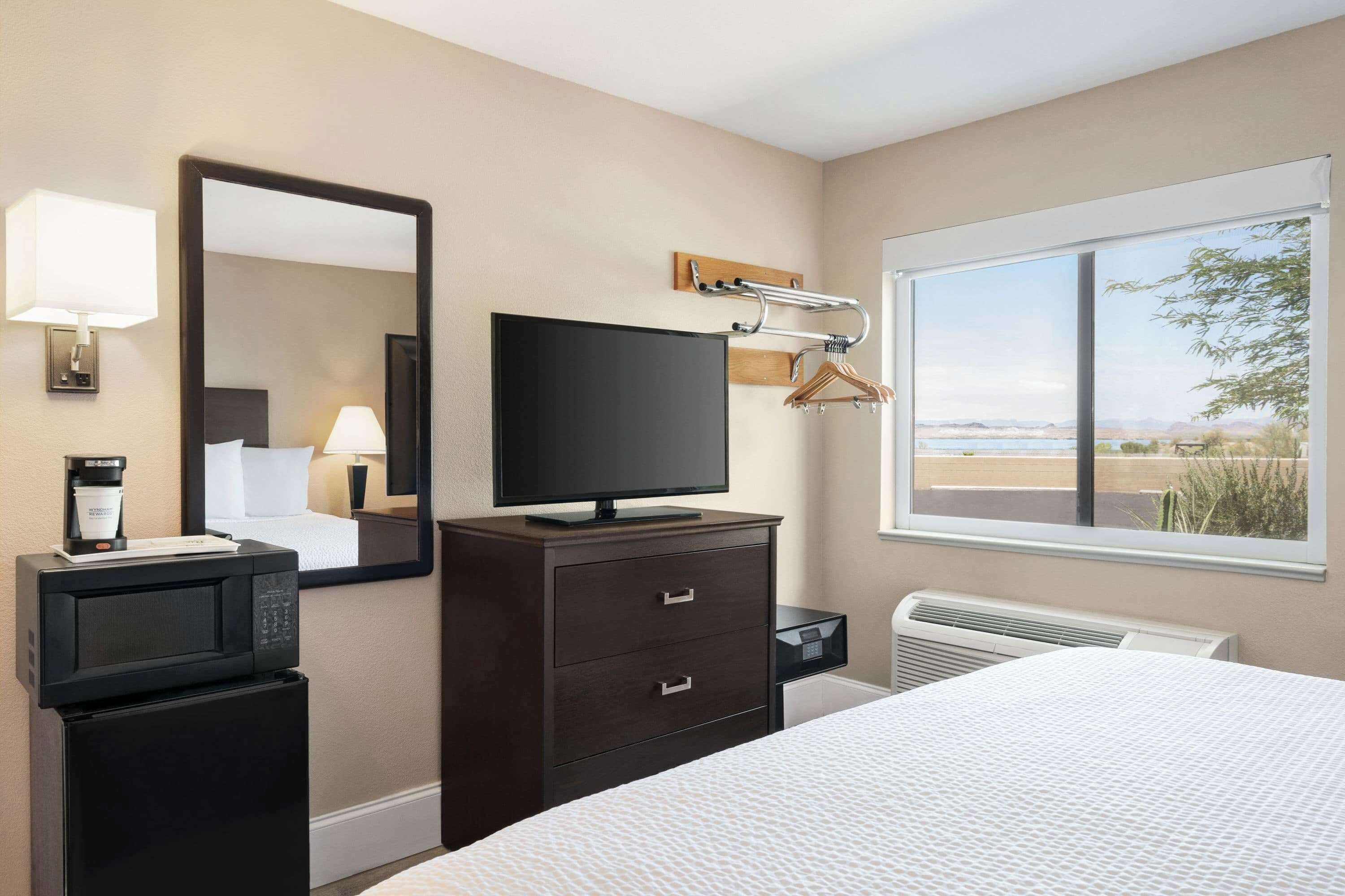 A hotel room with a bed, a TV, a dresser, a mirror, a window with a view, and a heater.