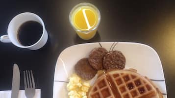 A plate with waffles, sausage, scrambled eggs, and a cup of coffee on a table.
