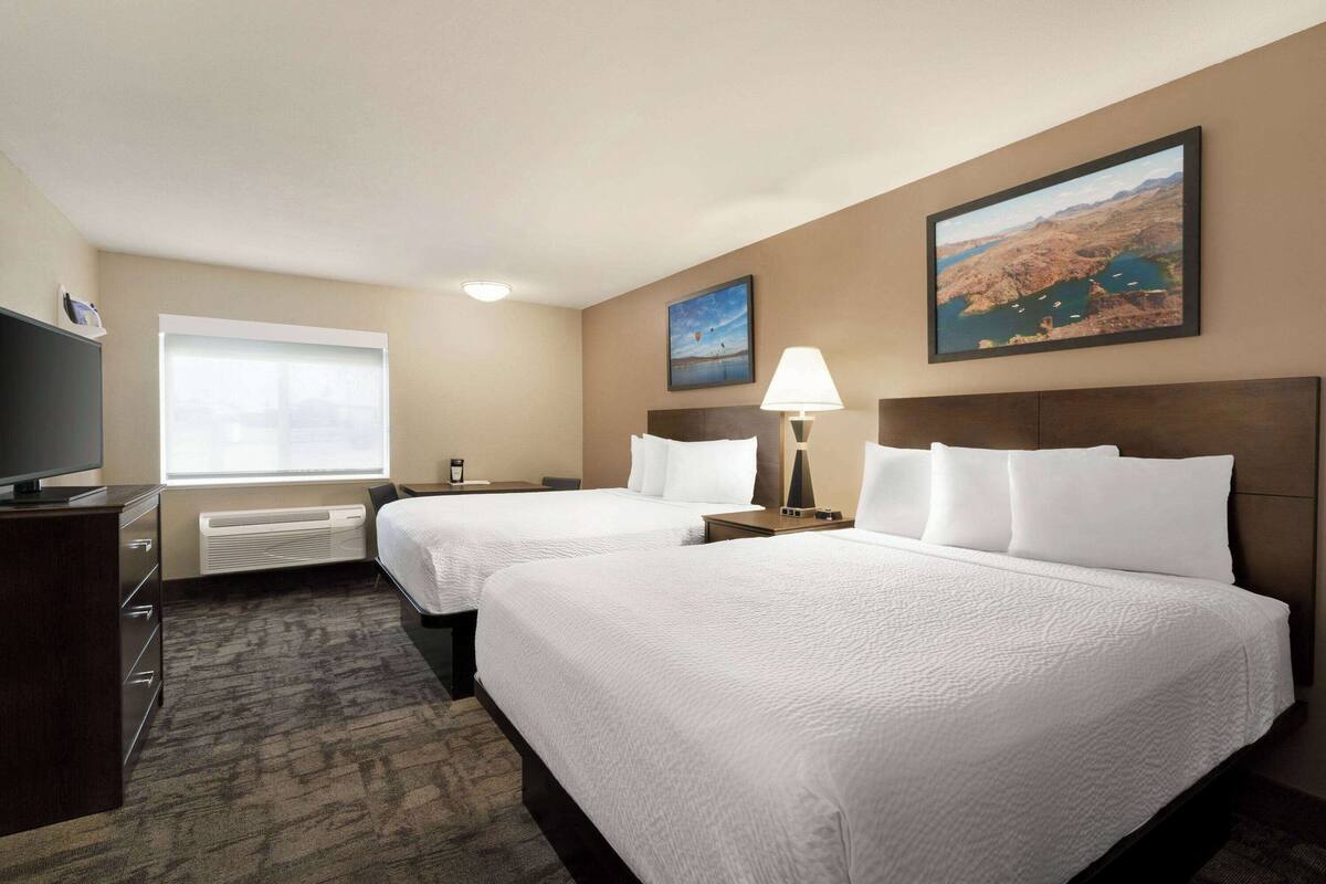 A hotel room with two beds, a TV, a window, and a painting on the wall.