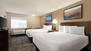 A hotel room with two beds, a TV, a window, and a painting on the wall.
