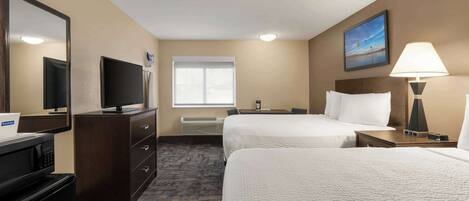 A hotel room with two beds, a desk, a television, a mirror, a window, and a lamp.