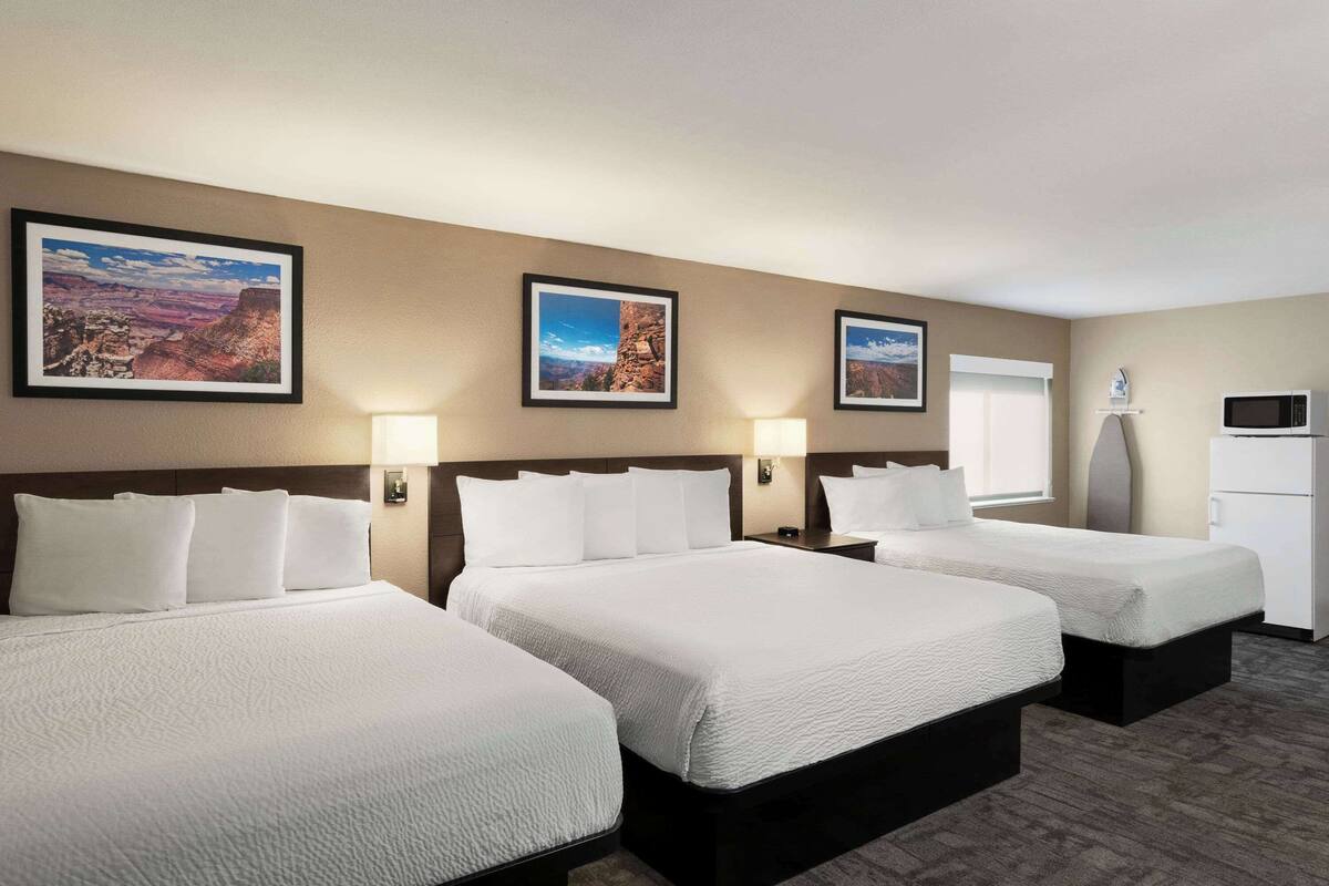 A hotel room with three beds, a microwave, and a refrigerator.