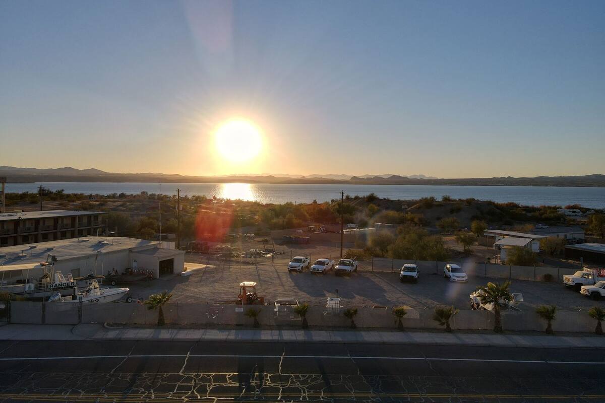 A parking lot with several cars, a boat named 'RANGER PARKS,' and a body of water with mountains in the background.