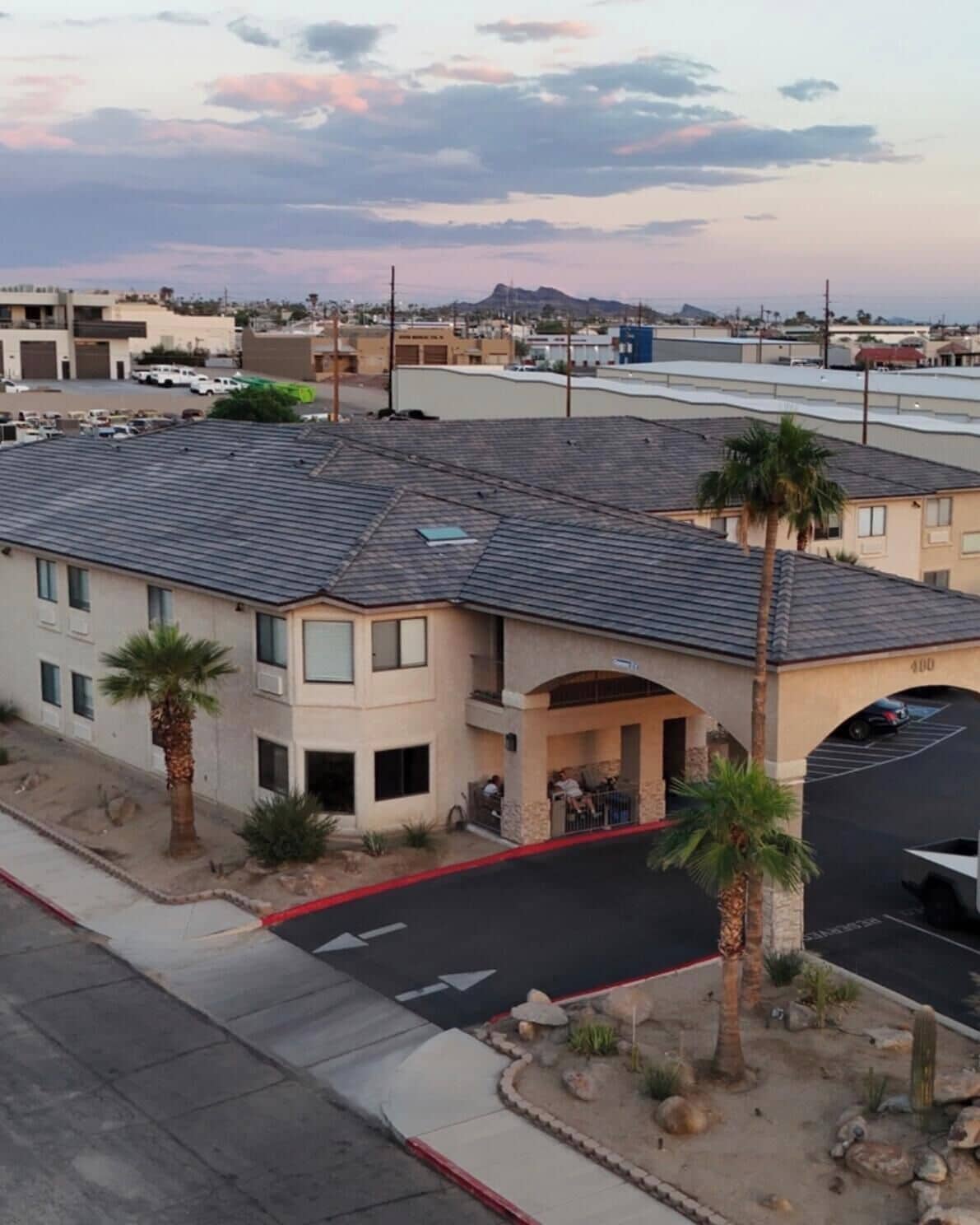 A multi-story building with a parking lot, palm trees, and a clear sky.