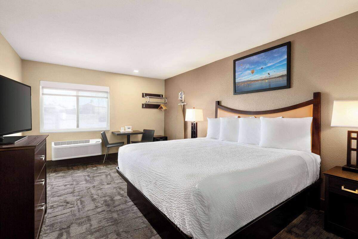 A hotel room with a large bed, a desk, a chair, a television, and a painting on the wall.