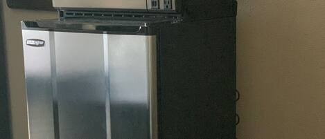 A compact refrigerator with a microwave on top, located in a corner of a room with a carpeted floor.