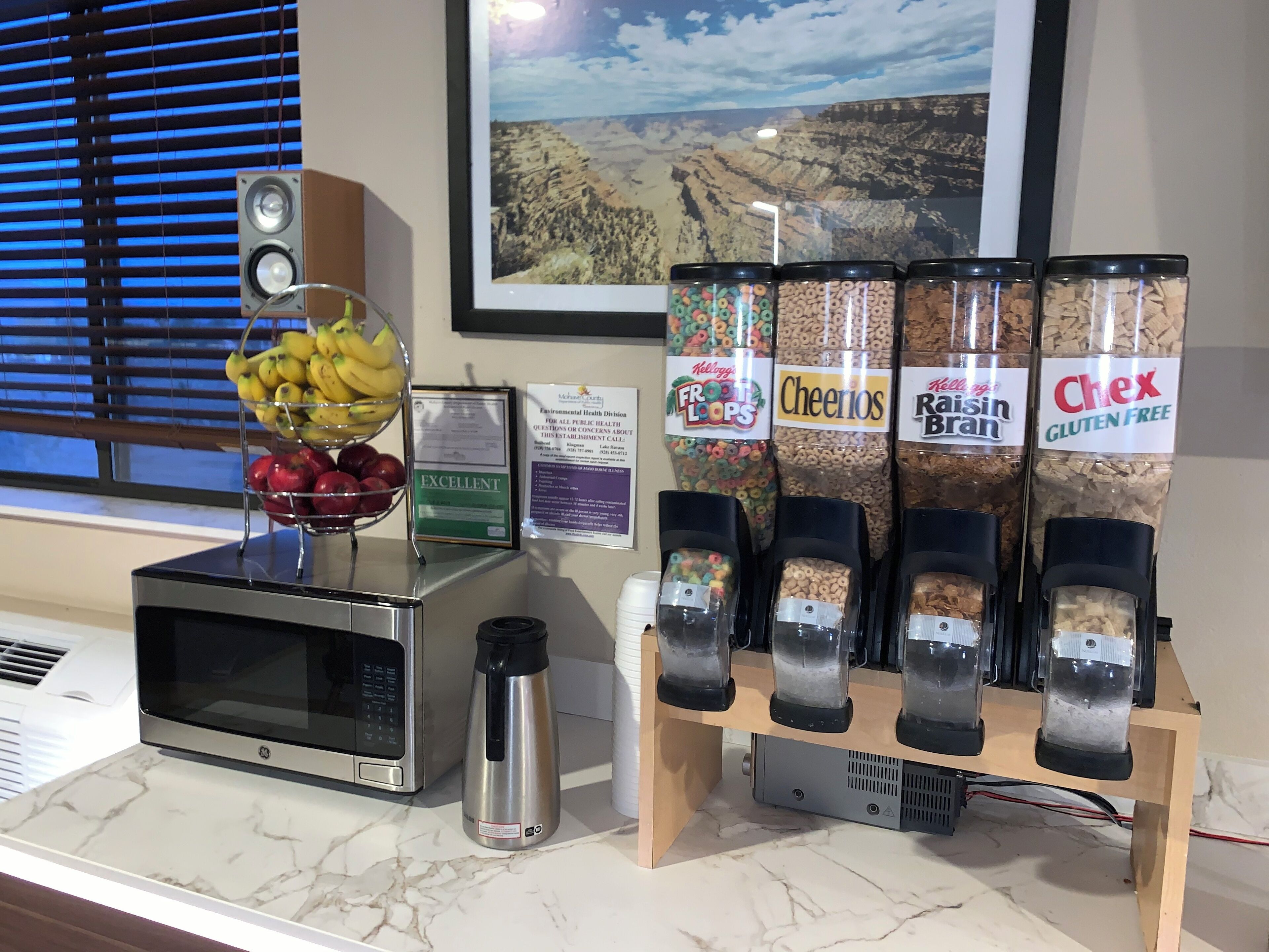 Una barra de desayuno con dispensadores de cereales, un frutero, un microondas y un dispensador de agua.