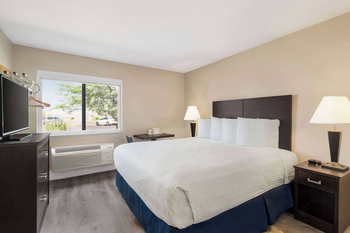 A hotel room with a large bed, bedside lamps, a TV, and a window with a view of the outside.