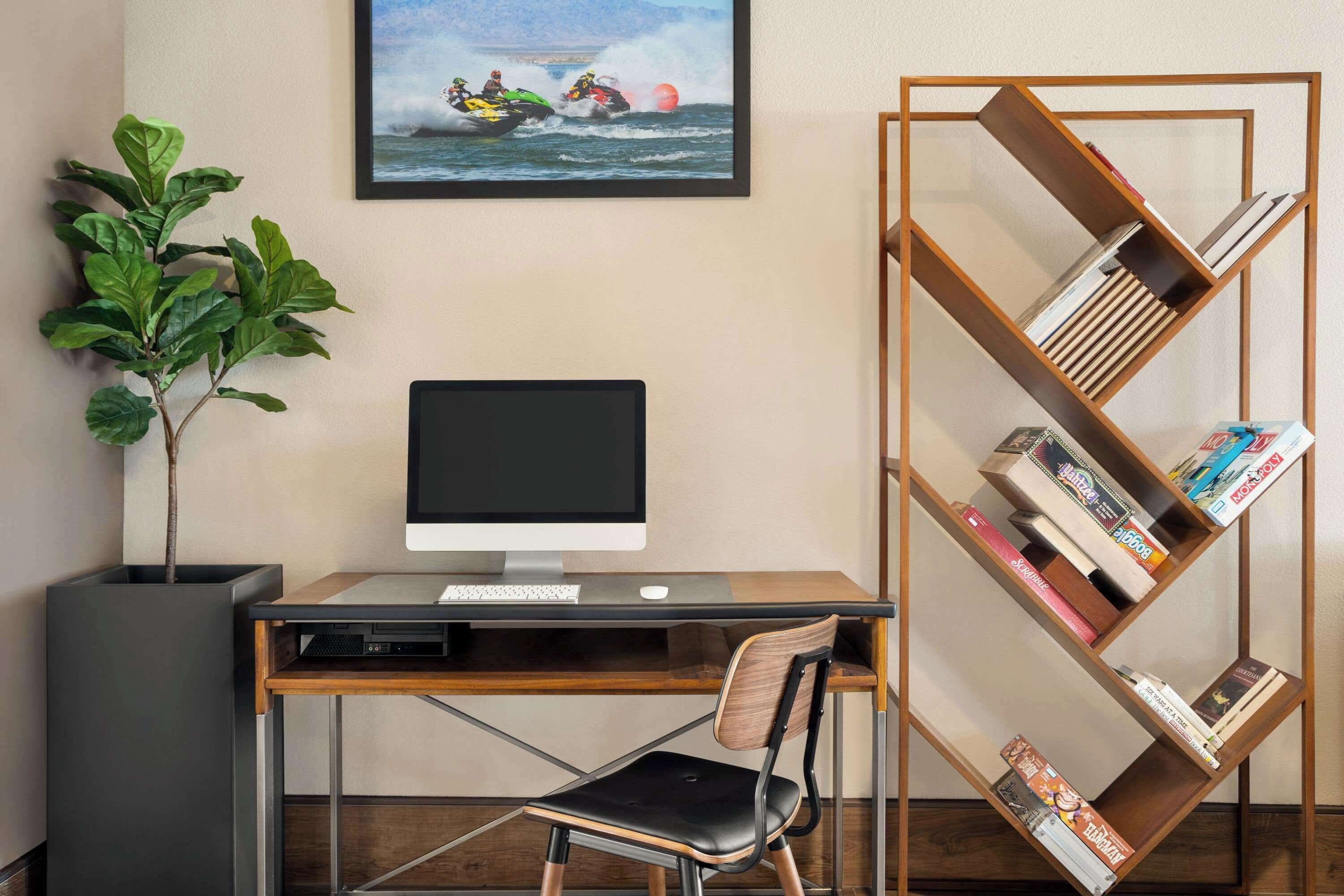 A modern office space with a desk, computer, chair, bookshelf, and a potted plant.