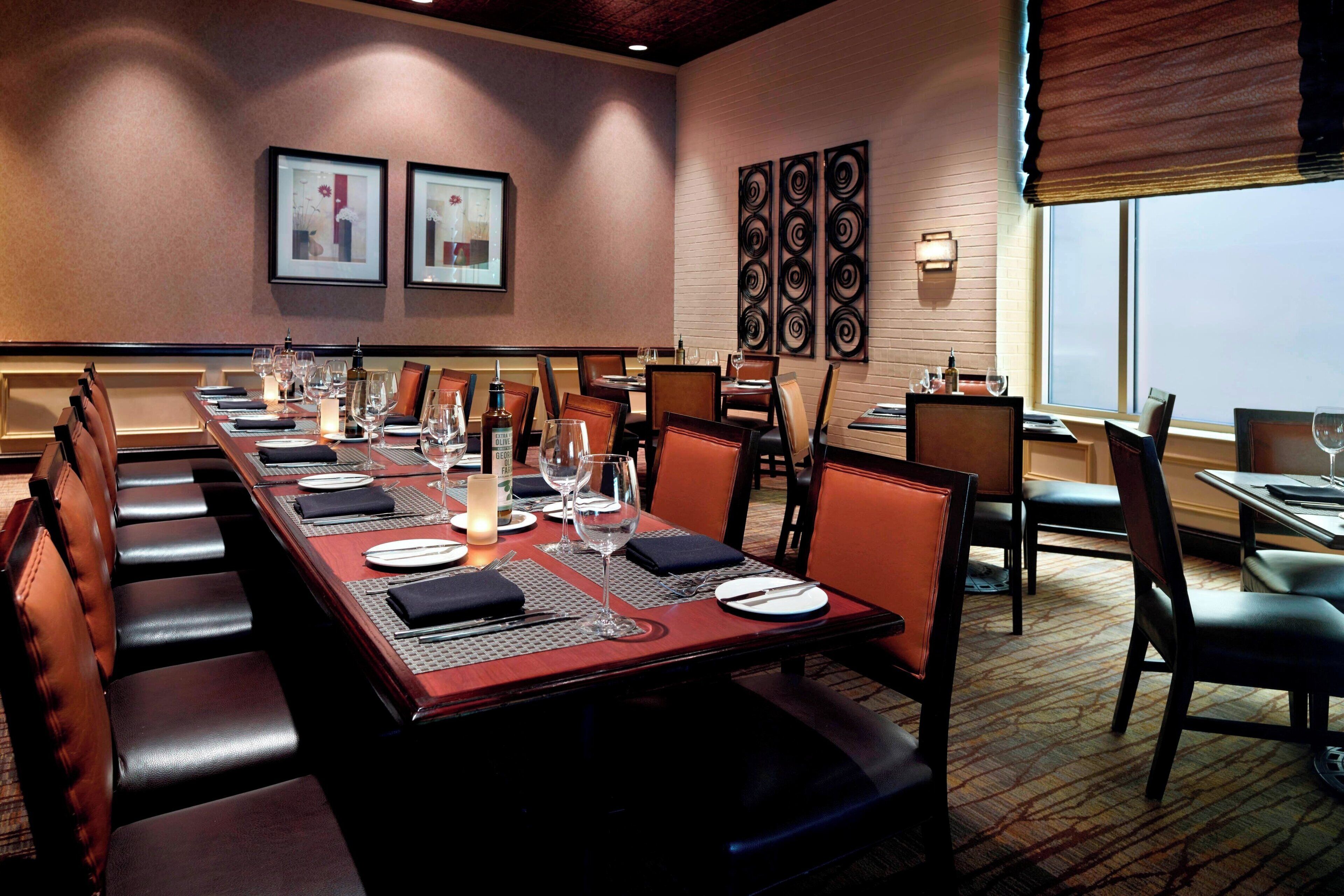 A dining area with a long table set for multiple guests, cushioned seating, and framed artwork on the walls.