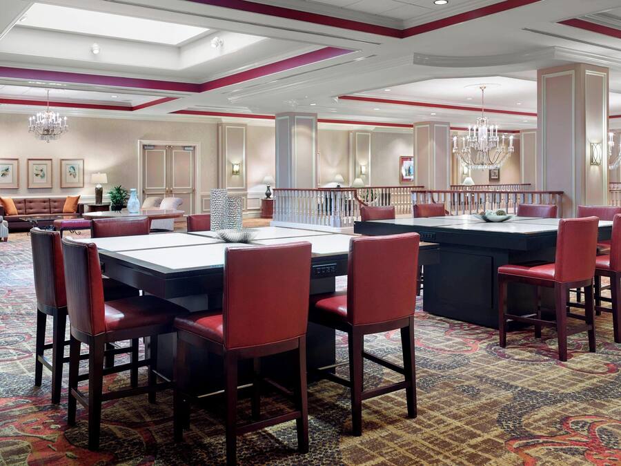 Ein Hotel-Speisesaal mit einem großen Tisch, rot gepolsterten Stühlen, Kronleuchtern und einem gemusterten Teppich.