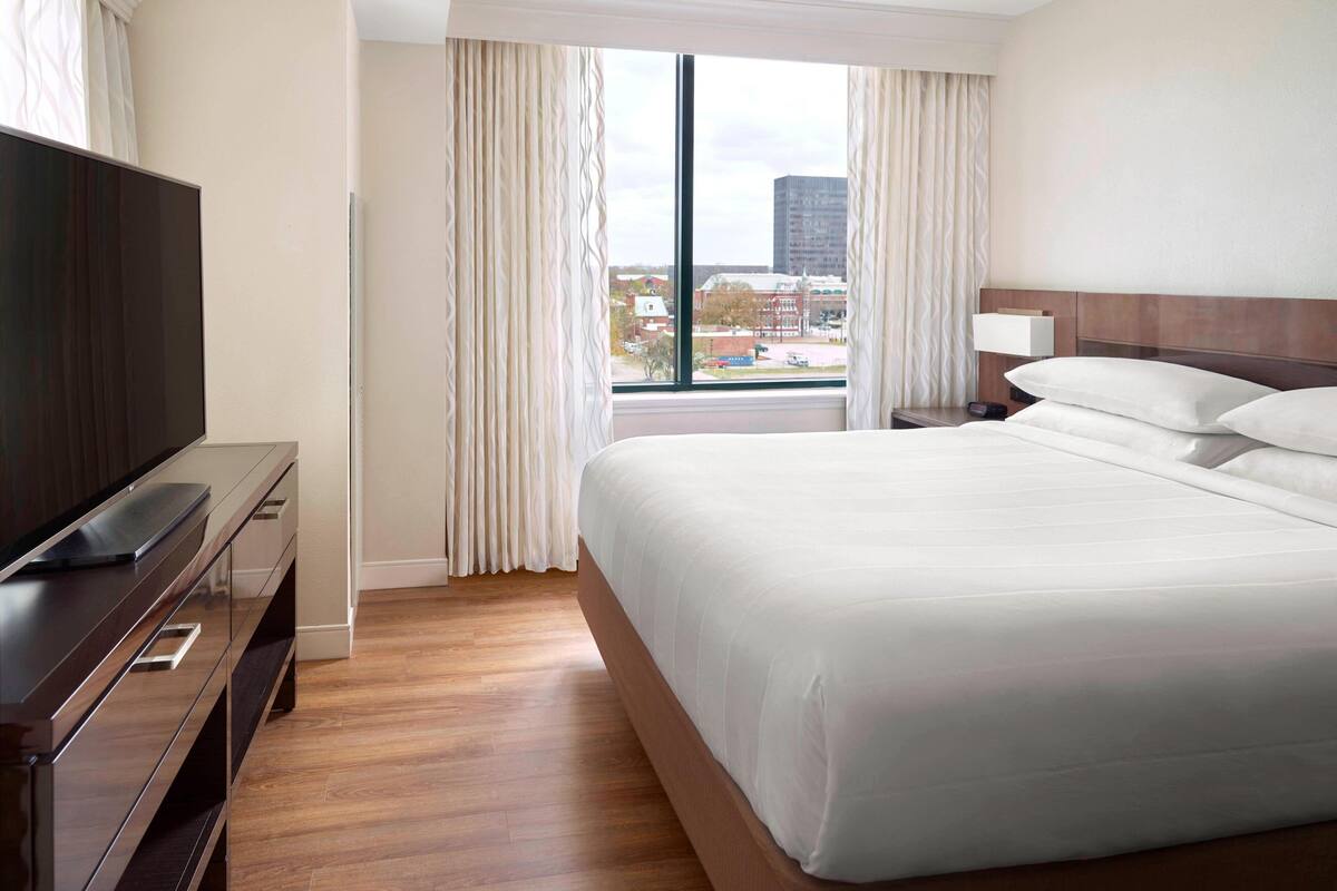 A hotel room with a large bed, a TV on a wooden dresser, and a window with curtains.