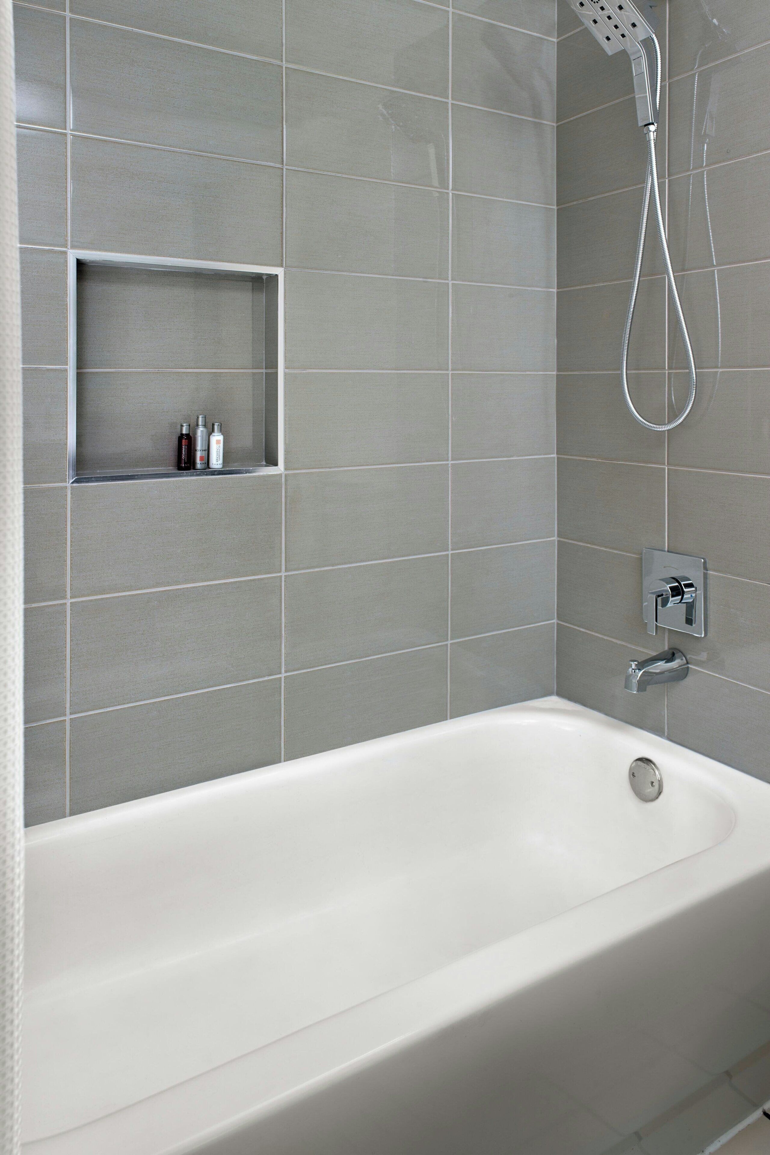 Un baño moderno con una bañera blanca, un cabezal de ducha y un estante con artículos de aseo.