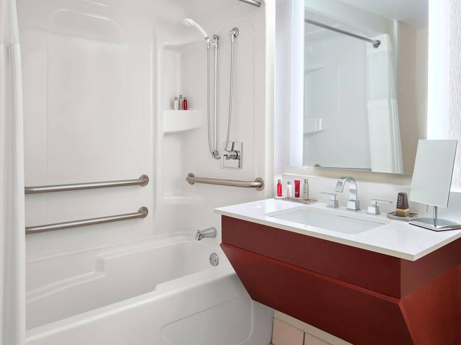 Une salle de bain moderne avec une baignoire blanche, un meuble-lavabo rouge, un grand miroir et un espace douche doté d’une porte en verre.