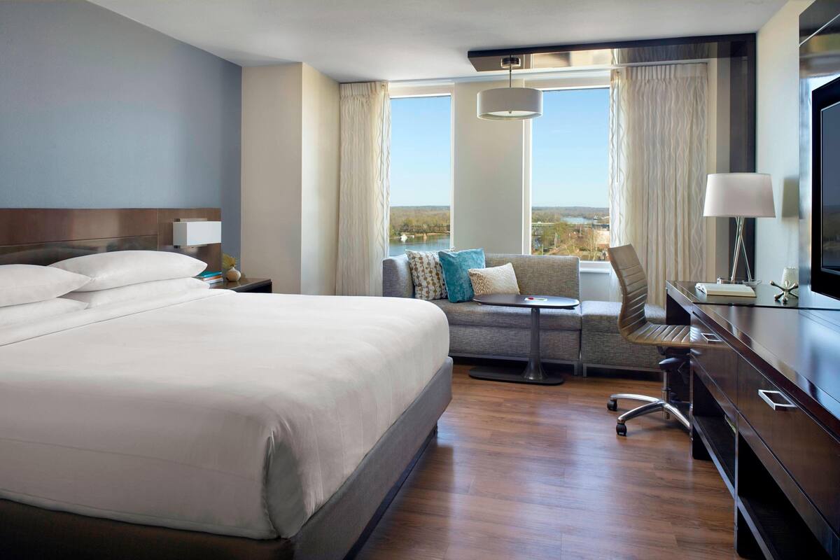 A hotel room with a large bed, a sofa, a desk, and a TV.