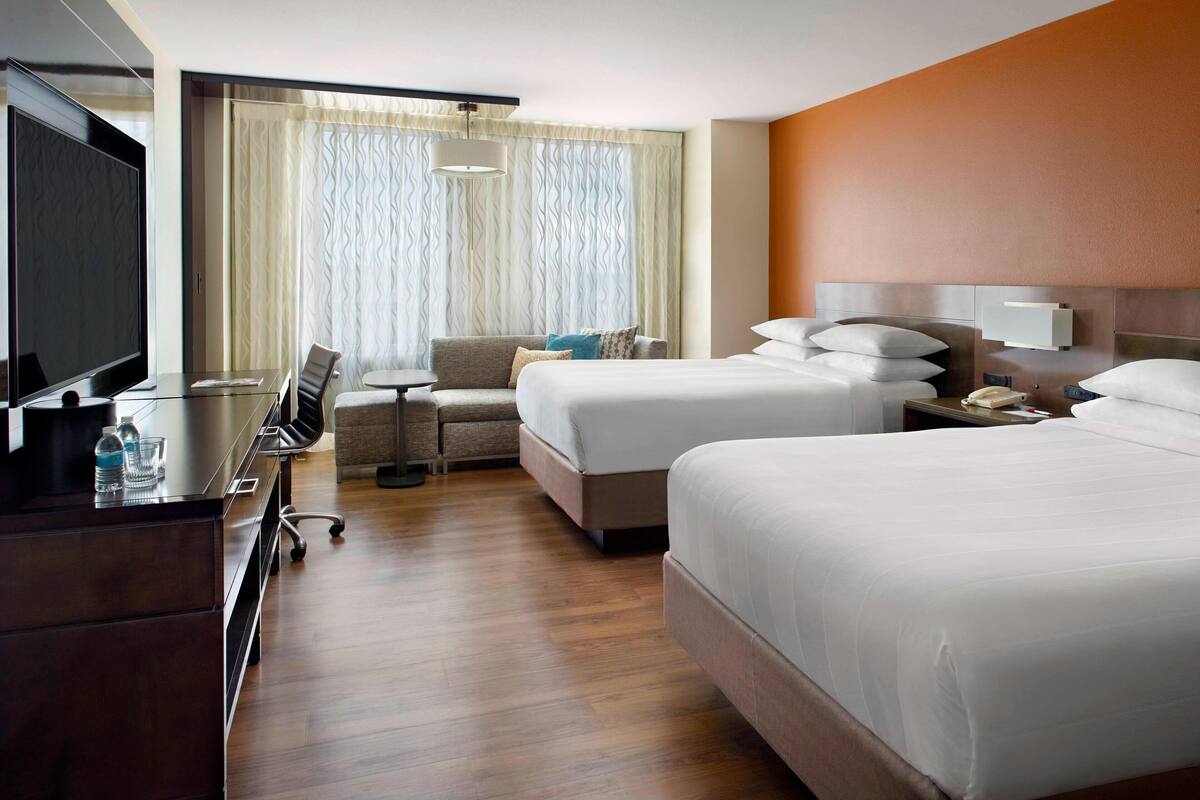 A hotel room with a large bed, a smaller bed, a desk with a TV, and a sofa.