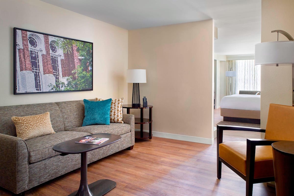 A hotel room with a sofa, a small table, a lamp, and a chair.