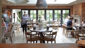 A spacious cafe with large windows, wooden furniture, and a modern pendant light. - No 38 The Park (Cheltenham)