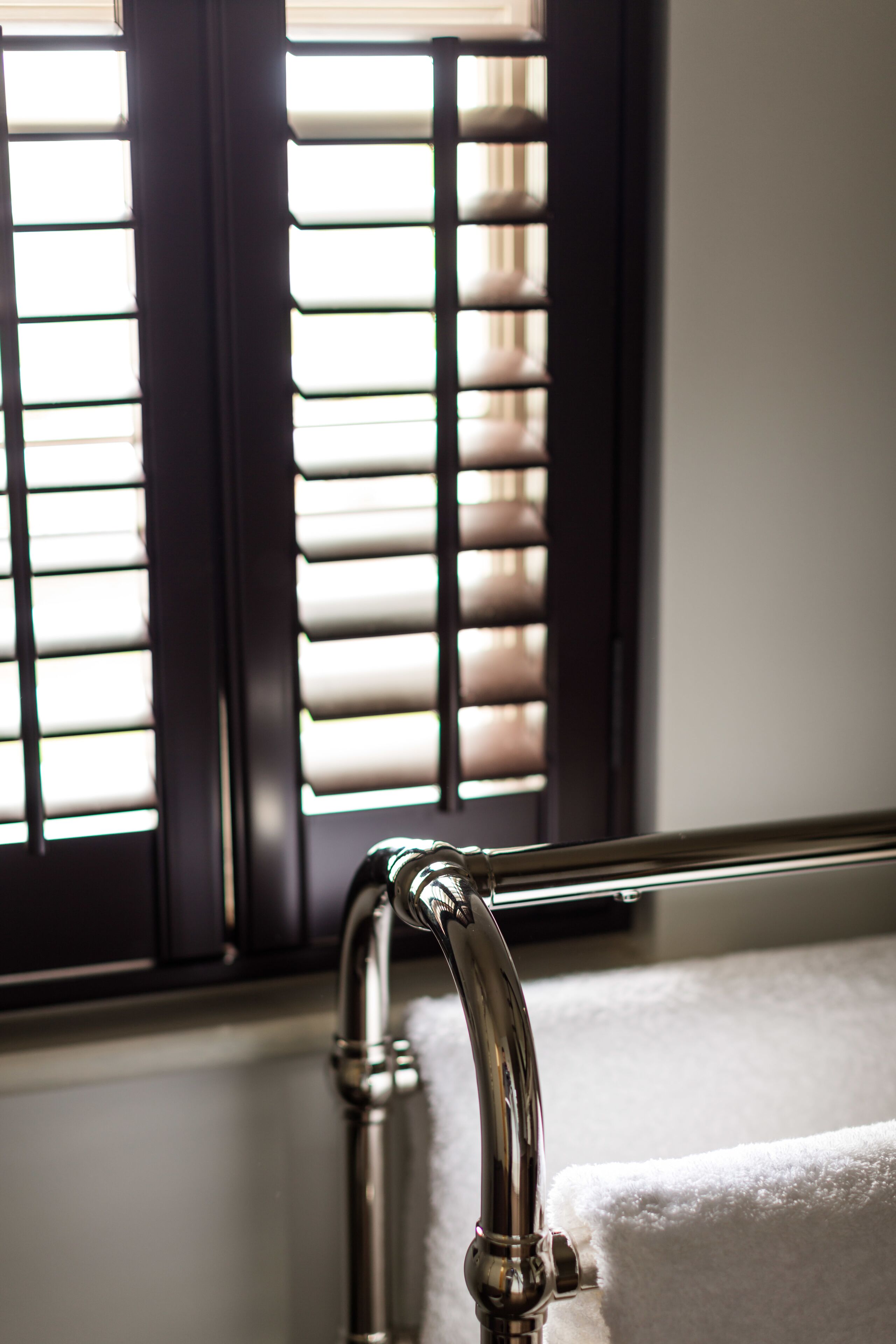 A bathroom with a towel rack, a faucet, and a window with blinds.