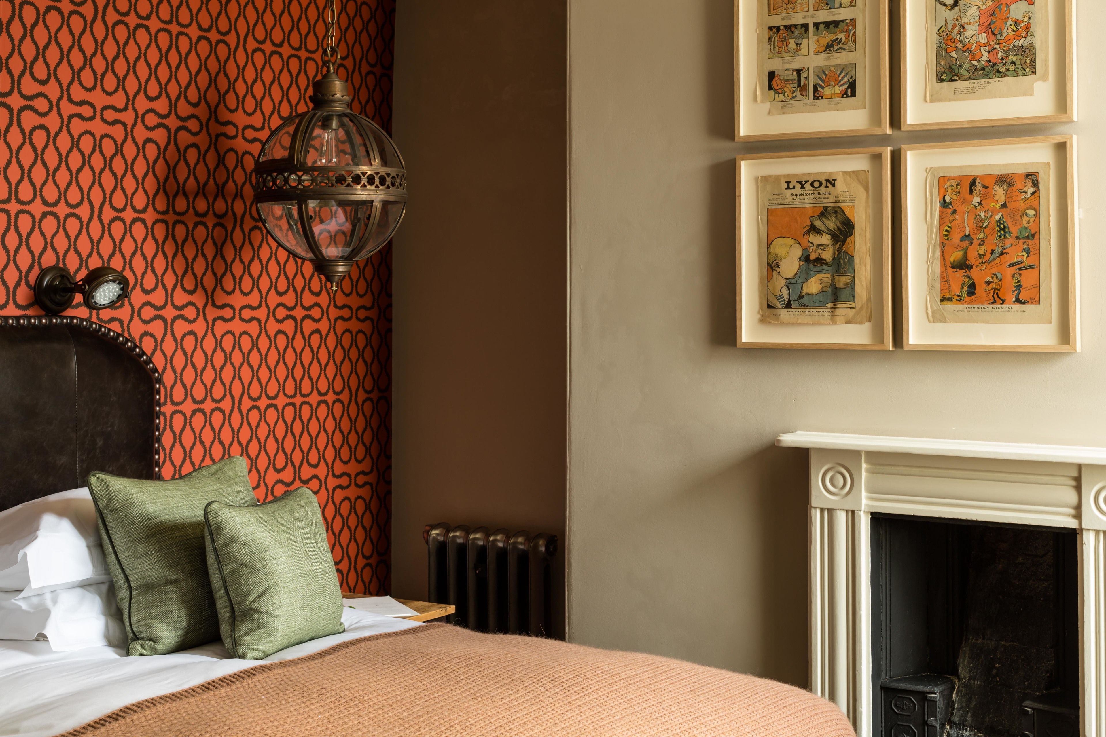 A bedroom with a patterned wall, a bed with pillows, a hanging lamp, and framed pictures on the wall.
