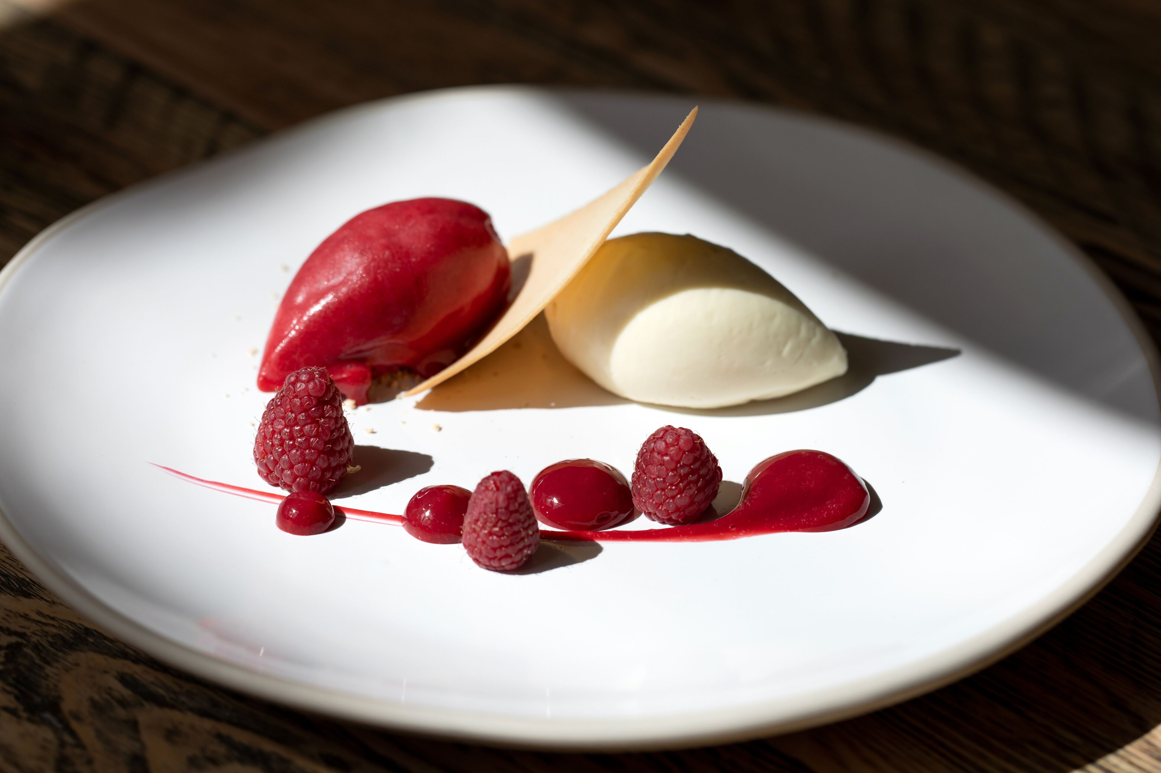 A dessert plate with a scoop of ice cream and raspberries.