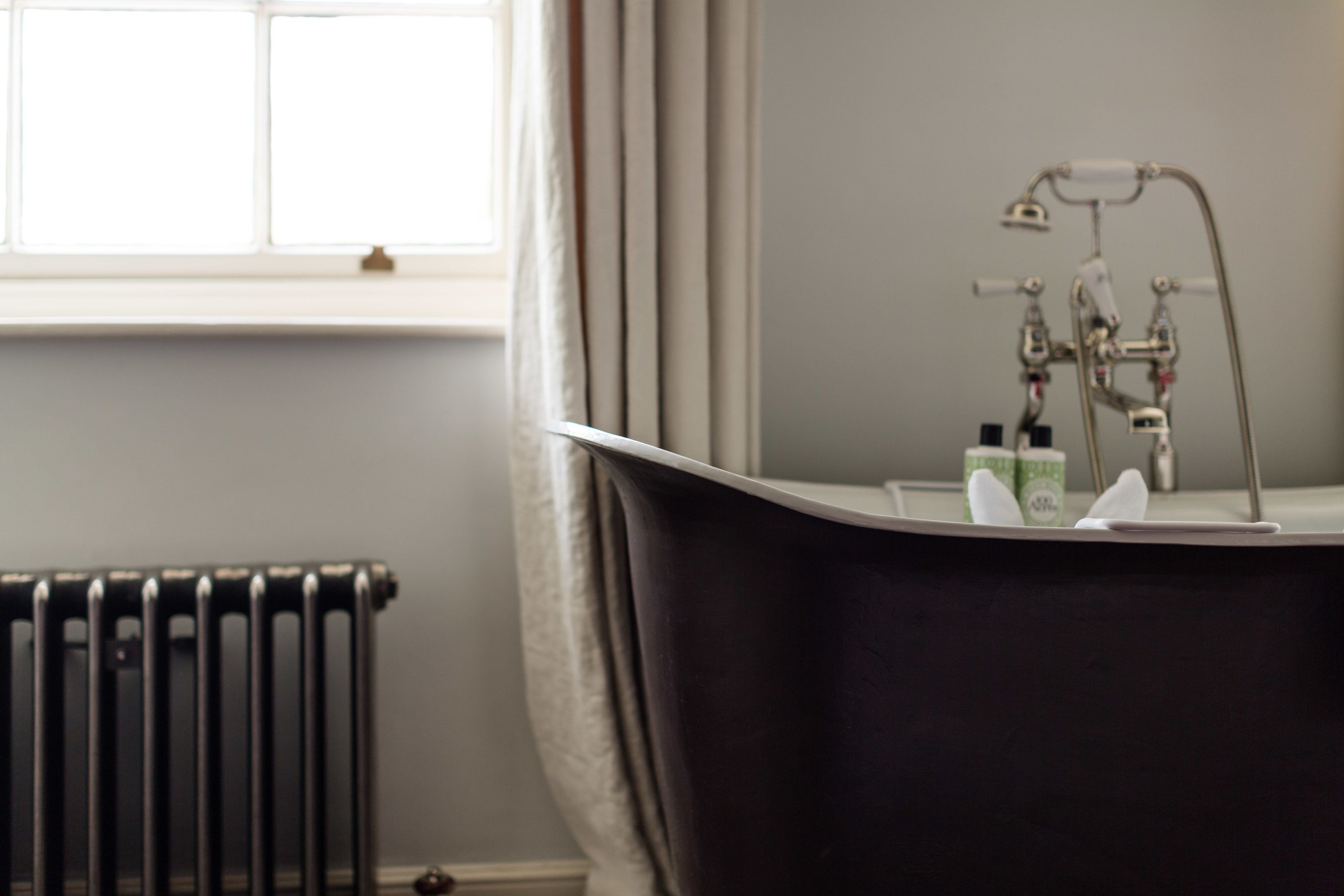 A bathroom with a freestanding bathtub, a radiator, and a window with curtains.