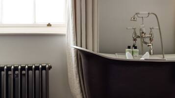 A bathroom with a freestanding bathtub, a radiator, and a window with curtains.