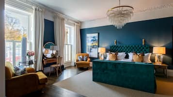 A modern bedroom with a teal upholstered headboard, a wooden desk, a yellow armchair, and a large window with curtains.
