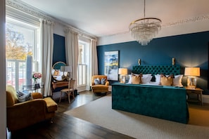 Quarto moderno com cabeceira estofada em tons de verde-água, escrivaninha de madeira, poltrona amarela e uma grande janela com cortinas.