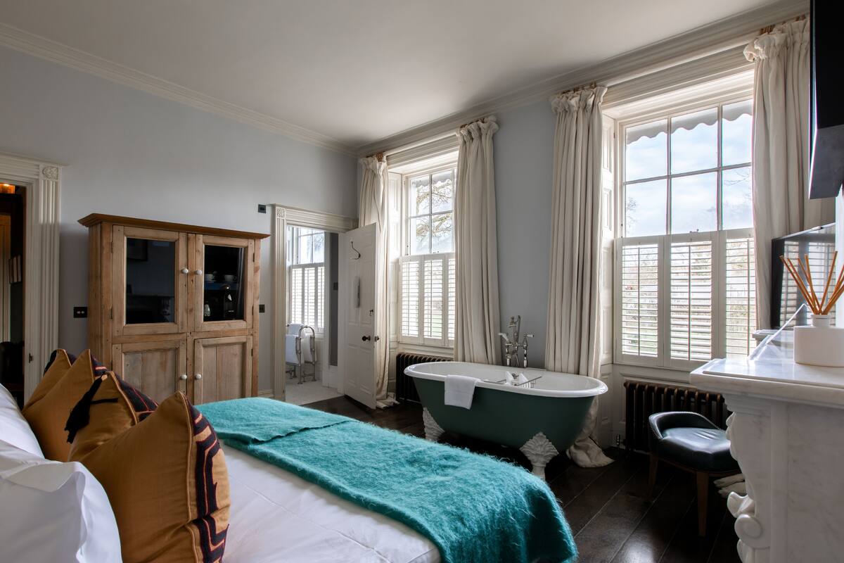 Un dormitorio con una cama grande, una bañera antigua de patas de león y un armario de madera.