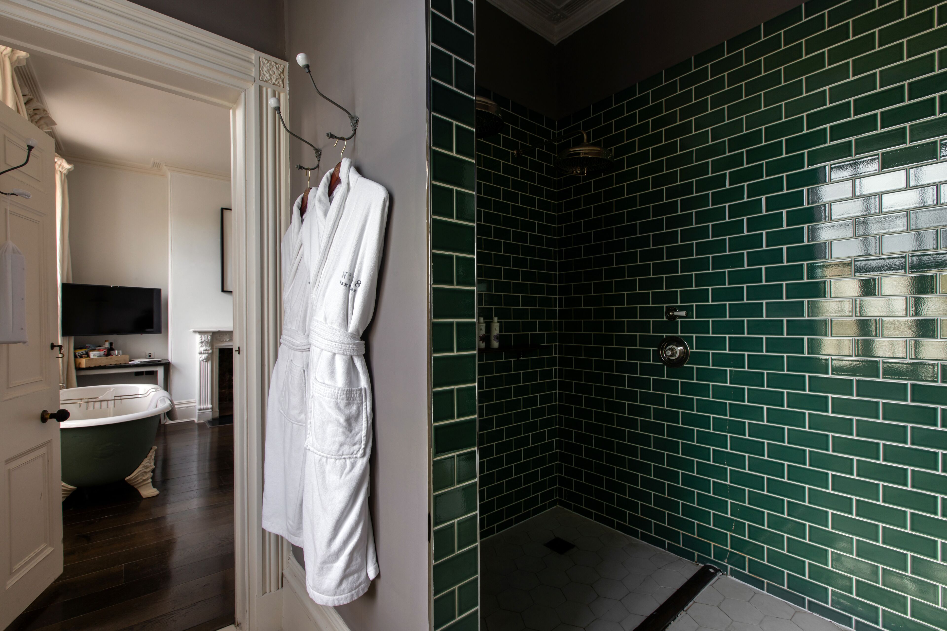 Un baño con bañera, una bata blanca colgada en la pared y una zona de ducha con azulejos verdes.