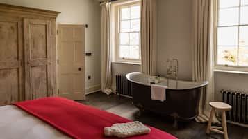 Una habitación con una cama grande, una bañera antigua y un ventanal con cortinas.