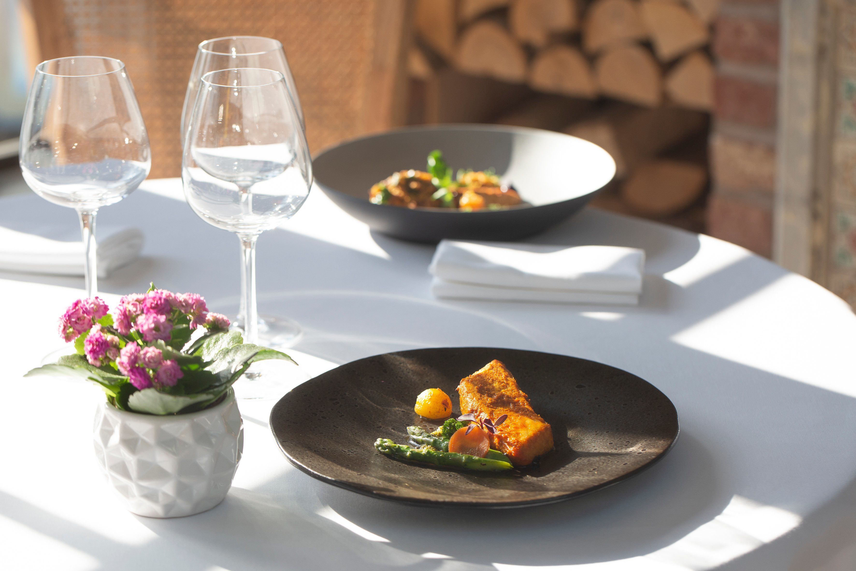 Una mesa con un plato de comida, dos copas de vino y un jarrón con flores.