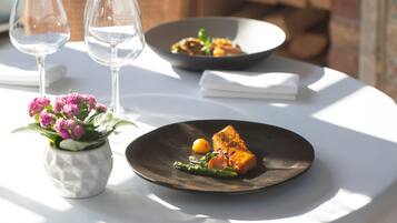Una mesa con un plato de comida, dos copas de vino y un jarrón con flores.