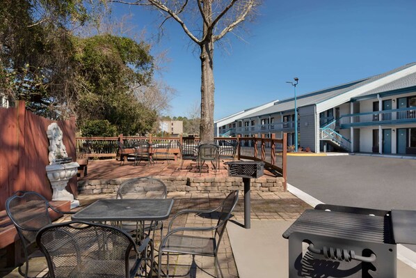 Un patio exterior con mesas y sillas de metal, una parrilla y una jardinera de piedra.