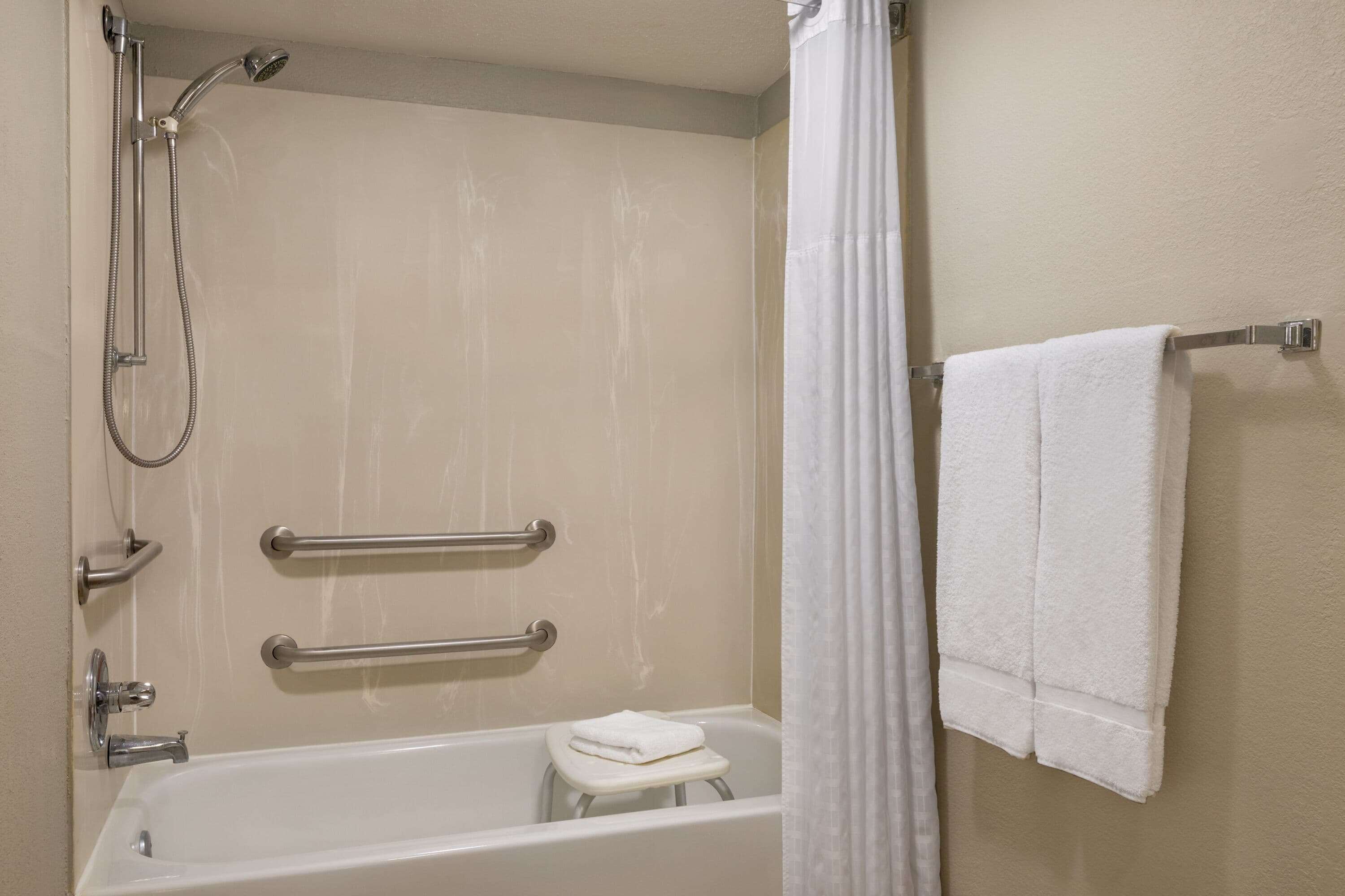 Un baño con bañera, ducha, barras de apoyo y un perchero para toallas.