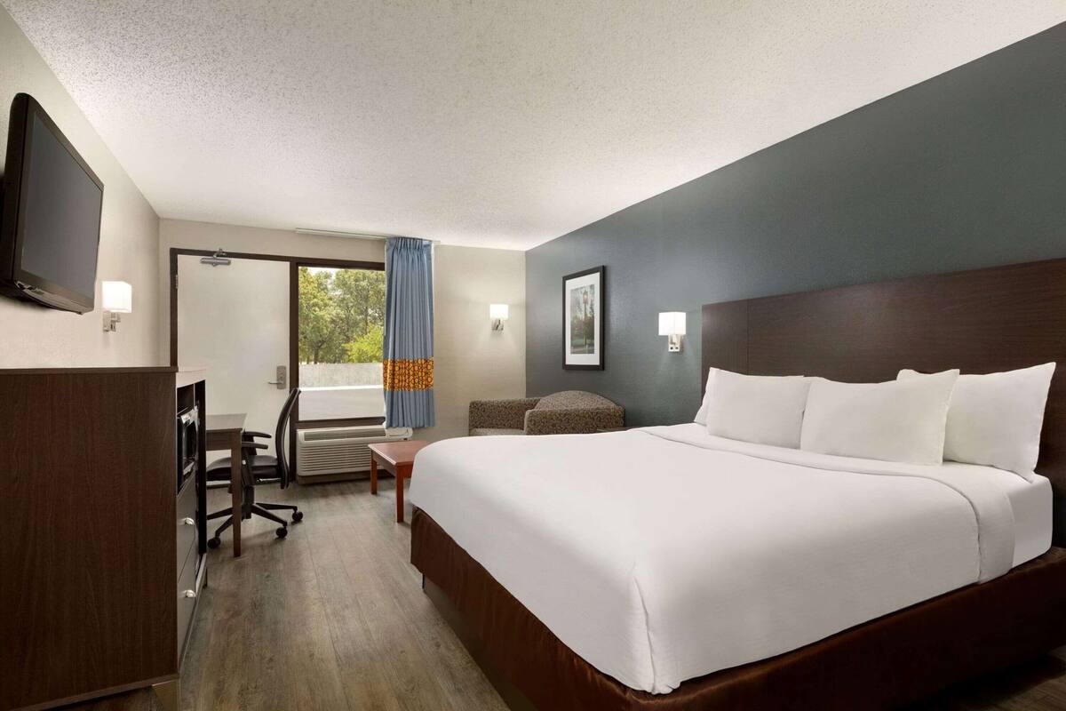 Quarto de hotel com cama, escrivaninha, cadeira e televisão.