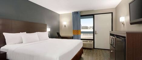 A hotel room with a large bed, a desk, a flat-screen TV, a minibar, and a window with a view.