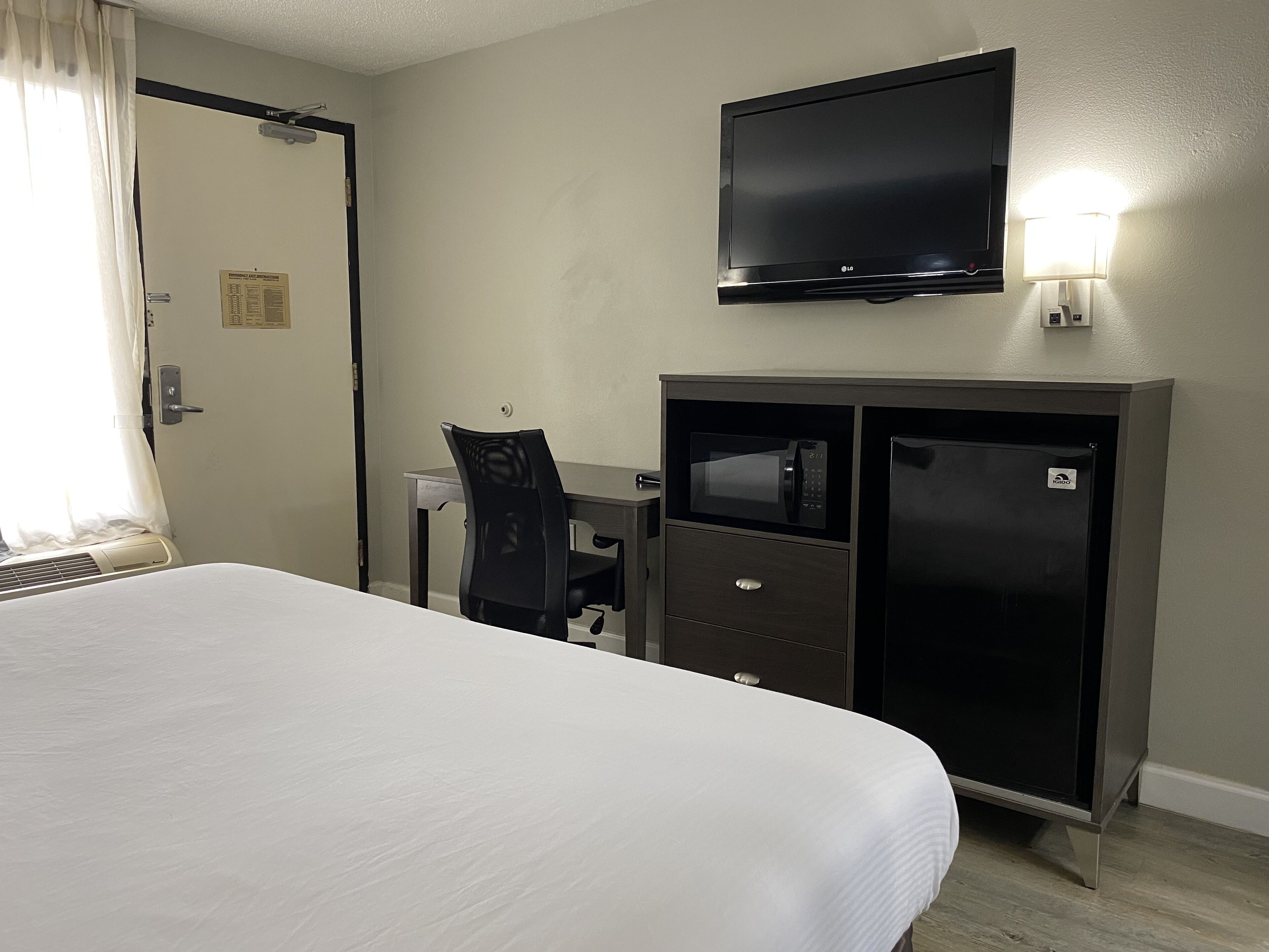 A hotel room with a bed, a desk with a chair, a TV mounted on the wall, and a minibar.